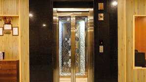 Un ascenseur doté de panneaux en bois et d’une porte en verre ornée de motifs décoratifs.