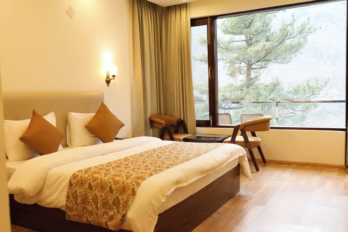 A hotel room with a large bed, a desk, and a view of trees through a window.
