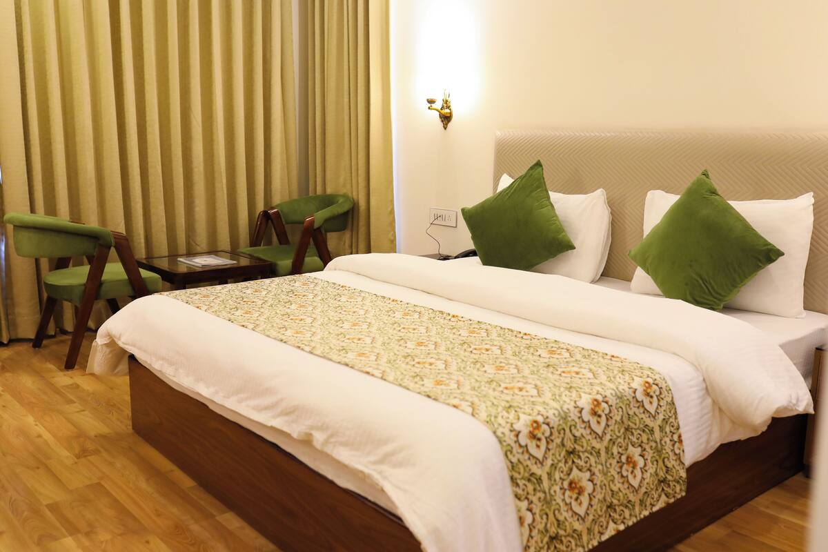 A neatly made bed with a patterned bedspread, two green pillows, and a bedside table with a lamp.