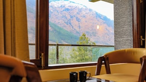 Une pièce avec vue sur une montagne, une fenêtre avec des rideaux, une table avec deux tasses et deux chaises.