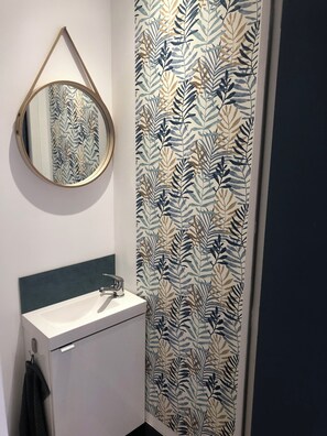 A bathroom with a white sink, a mirror, and a patterned wallpaper.