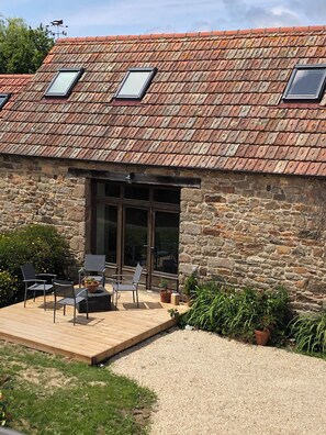 A stone building with a tiled roof, a wooden deck, and a seating area with chairs and tables.