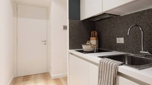 A modern kitchen with white cabinets, a black speckled backsplash, a stainless steel sink, and a pot on the stove. - Trieste Tranquil Tiny Haven (Trieste)
