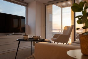 A modern living room with a flat-screen TV, a sofa, a chair, and a table with a bowl and a decorative item. - Ellinikon 360 Rooftop (Glyfada)