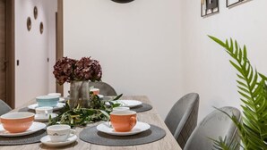 Un coin repas avec une table en bois dressée pour quatre personnes, entourée de chaises grises. Une grande horloge murale est fixée au-dessus de la table.