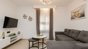 Un salon moderne avec un téléviseur à écran plat, un canapé gris, une petite table ronde et une console blanche.