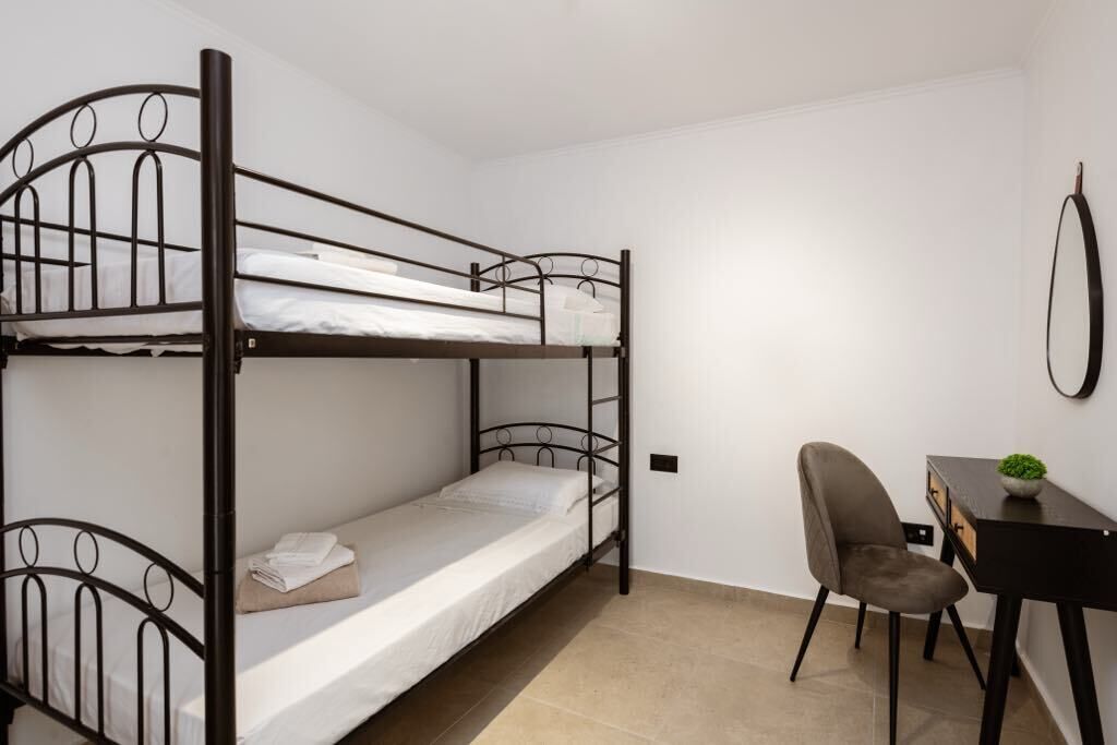 Een slaapkamer met een stapelbed, een bureau en stoel, een kleine plant en een spiegel aan de muur.