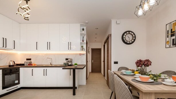 Une cuisine moderne avec des meubles blancs, un îlot central et un coin repas comprenant une table et des chaises en bois.