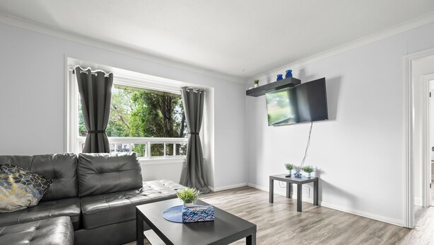 Una sala de estar moderna con un sofá de cuero, una mesa de centro, un televisor de pantalla plana montado en la pared y una mesita auxiliar con objetos decorativos.