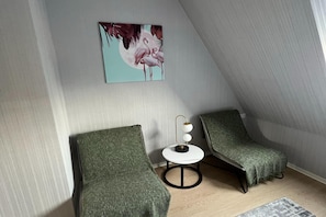 A room with a sloped ceiling, two green armchairs, a small white table with a lamp, and a painting of flamingos. - Comfortable 2-room Studio for 4 People, Dziwnow (Dziwnów)