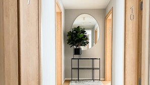 A hallway with wooden doors marked with numbers, a central plant on a console table, and a grey carpet. - Comfortable 2-room Studio for 4 People, Dziwnow (Dziwnów)