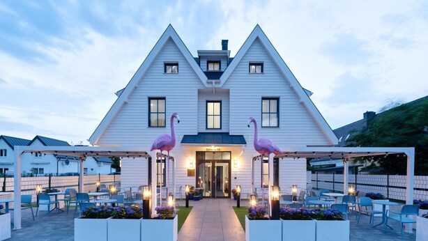 A white building with a triangular roof, two pink flamingos, and outdoor seating. - Comfortable 2-room Studio for 4 People, Dziwnow (Dziwnów)