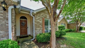 A brick house with a front door, a mailbox, and a tree in the yard.