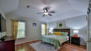 A bedroom with a bed, a ceiling fan, a nightstand, a dresser, and a window with curtains.