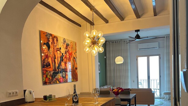 Une cuisine moderne avec un îlot central en bois, un grand tableau et un coin repas offrant une vue agréable.