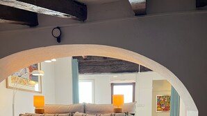Une chambre confortable avec un lit, des oreillers et une serviette, dotée d’un plafond rustique et offrant une vue sur la pièce adjacente.