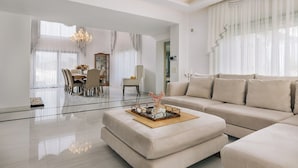 Ein geräumiges Wohnzimmer mit einer großen beigen Couch, einem Essbereich mit Tisch und Stühlen sowie einer Chandelier.