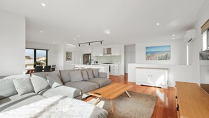 A modern living room with a sectional sofa, a wooden coffee table, and a kitchen in the background. - Surf Mist at Surf Beach (Surf Beach)