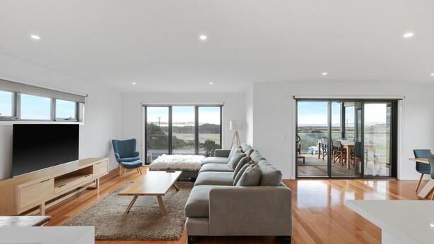 A modern living room with a large flat-screen TV, a sofa, a coffee table, and a view of the outdoors through large windows. - Surf Mist at Surf Beach (Surf Beach)