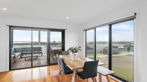 A spacious room with a wooden dining table, black chairs, and a potted plant. Large sliding glass doors lead to an outdoor seating area with a view of the countryside. - Surf Mist at Surf Beach (Surf Beach)