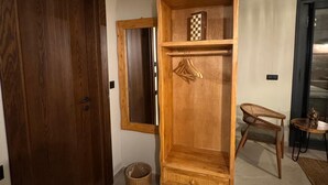 Un armario de madera con espejo, una mesita pequeña y una silla de mimbre en un pasillo.
