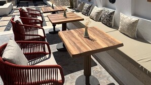 Un espacio al aire libre con sillas de mimbre y mesas de madera, paredes de piedra y decoración mural.