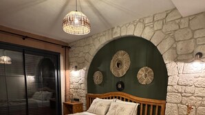 Un dormitorio con pared de piedra, estructura de cama de madera, un ventanal grande y una araña.