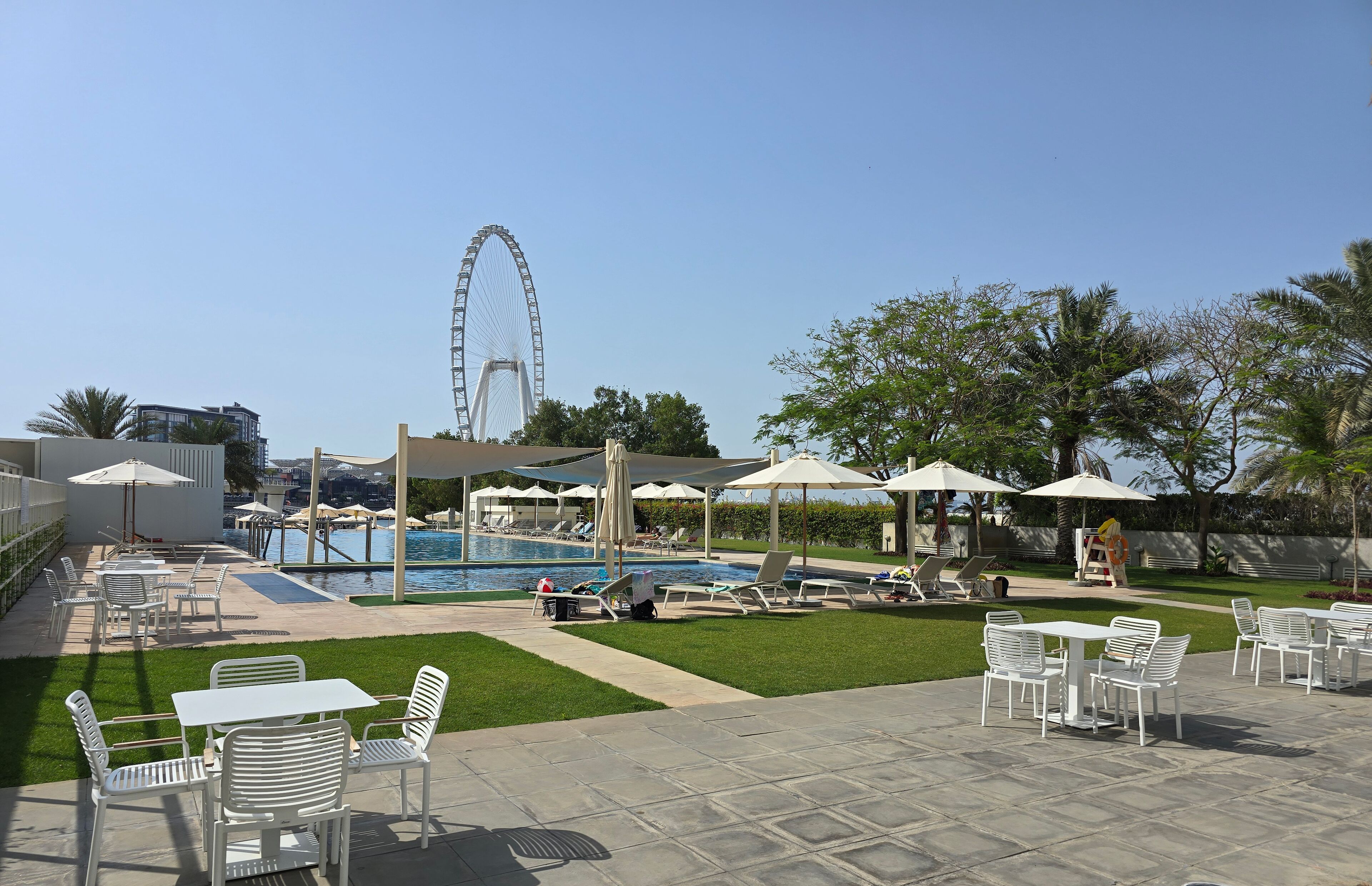 A pool area with lounge chairs, umbrellas, and a Ferris wheel in the background.