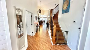 A spacious hallway with wooden flooring, a staircase with a railing, and a dining area in the background.