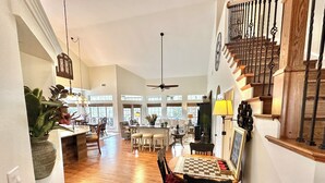 A spacious living area with a wooden floor, a dining table with chairs, a ceiling fan, and a staircase with a wooden railing.