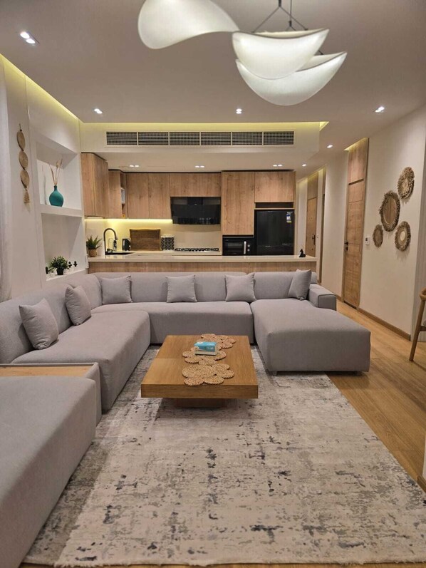 A modern living room with a sectional sofa, a coffee table, and a kitchen in the background.