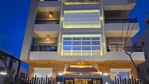 A multi-story building with a modern design, featuring balconies, large windows, and a well-lit entrance.