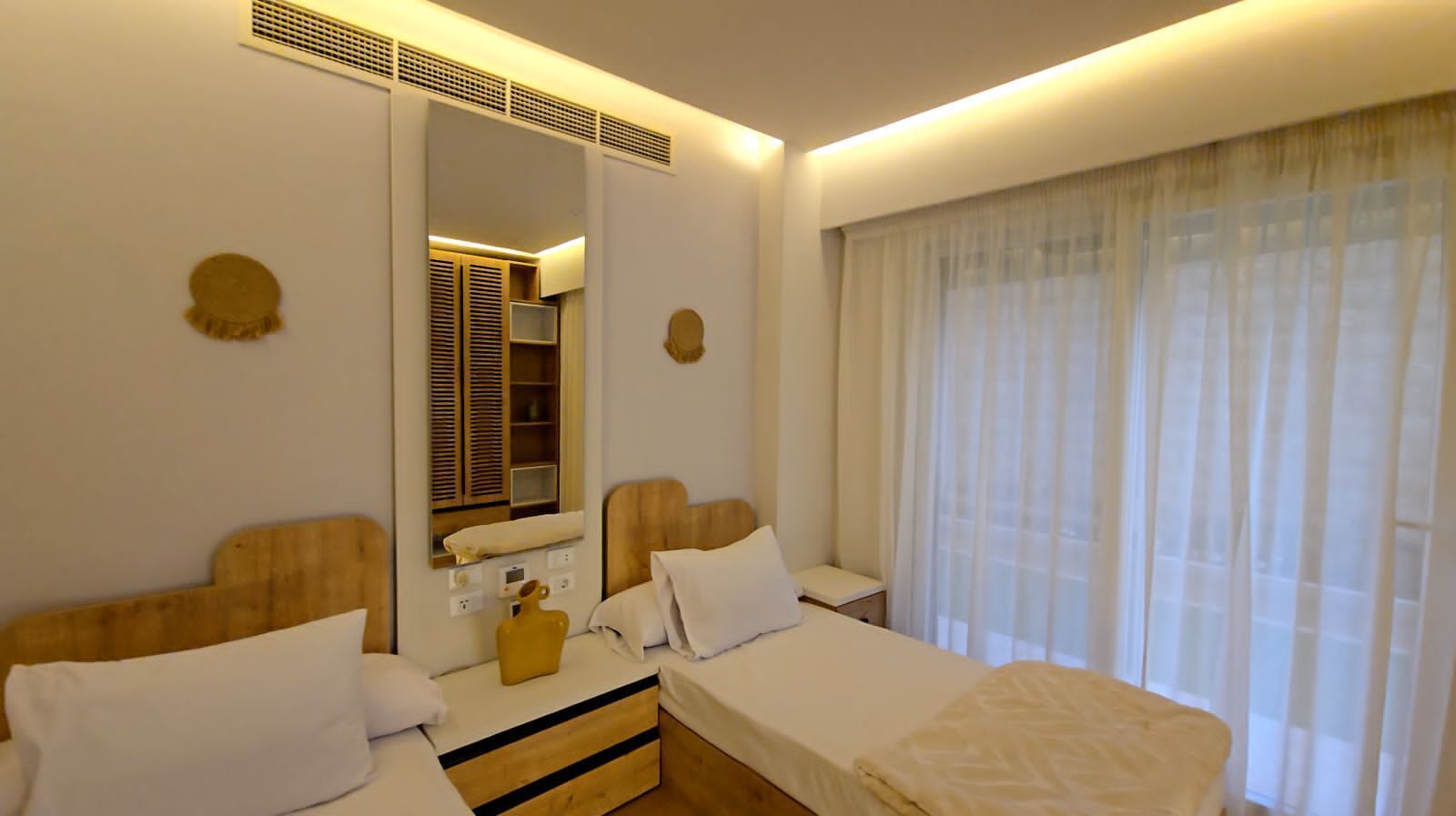 Ein Hotelzimmer mit zwei Betten, einem Schminktisch, einem Spiegel und einem großen Fenster mit Vorhängen.