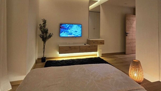 A modern bedroom with a bed, a TV mounted on the wall, a bedside table, and a nightstand.