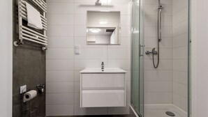 Un baño moderno con inodoro, lavamanos con espejo, toallero y ducha con mampara de vidrio.