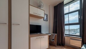 Habitación moderna con televisión, escritorio y ventana grande con cortinas.