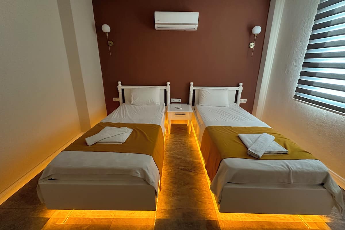 A twin room with two beds, a nightstand, an air conditioning unit, and a window with blinds.