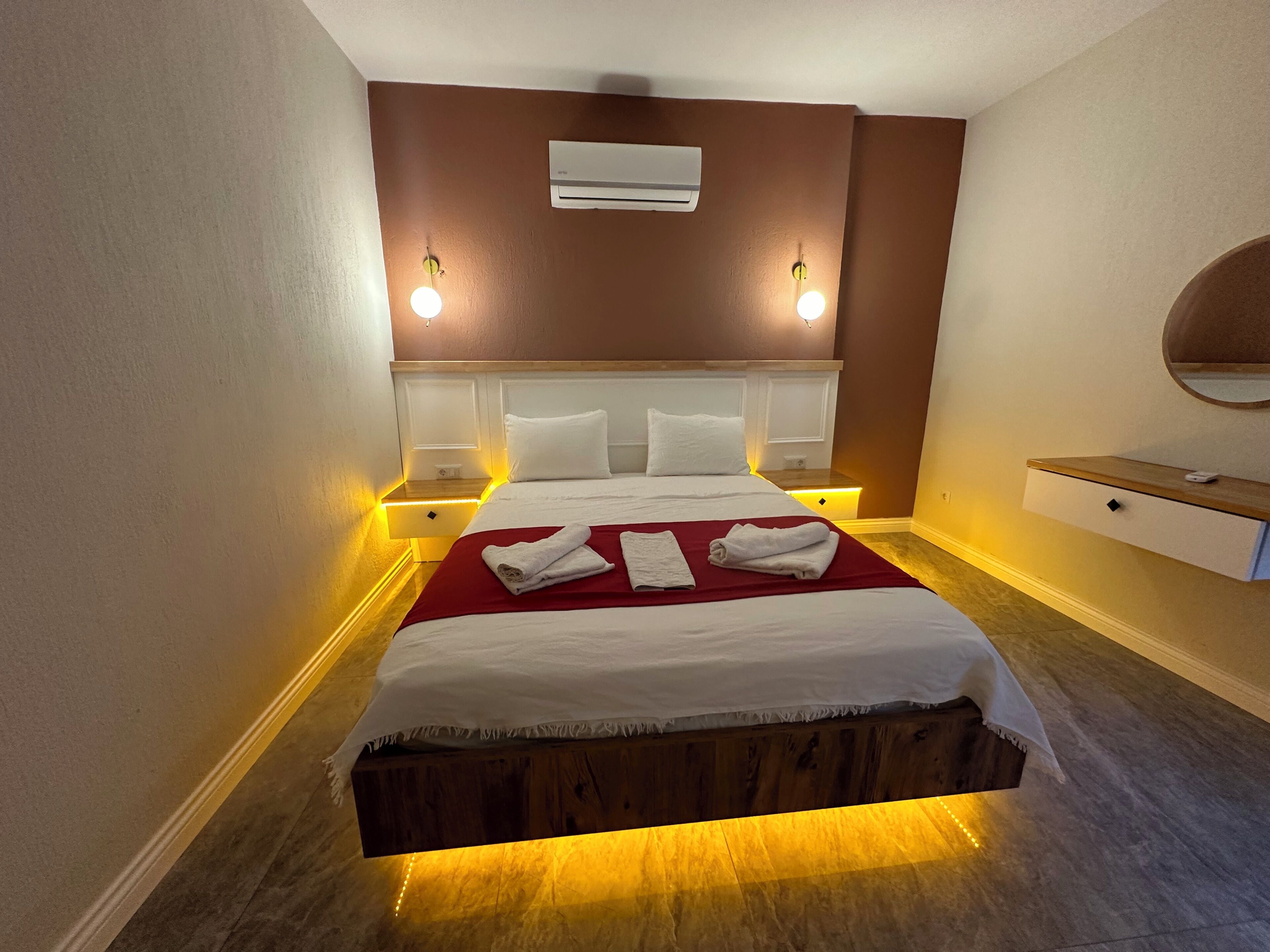 Una habitación de hotel con cama, lámparas de noche, aire acondicionado, mesita de noche y espejo.