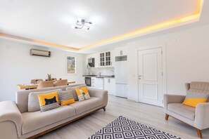 Een moderne woonkamer met een bank, fauteuil, eettafel en keukenhoek.