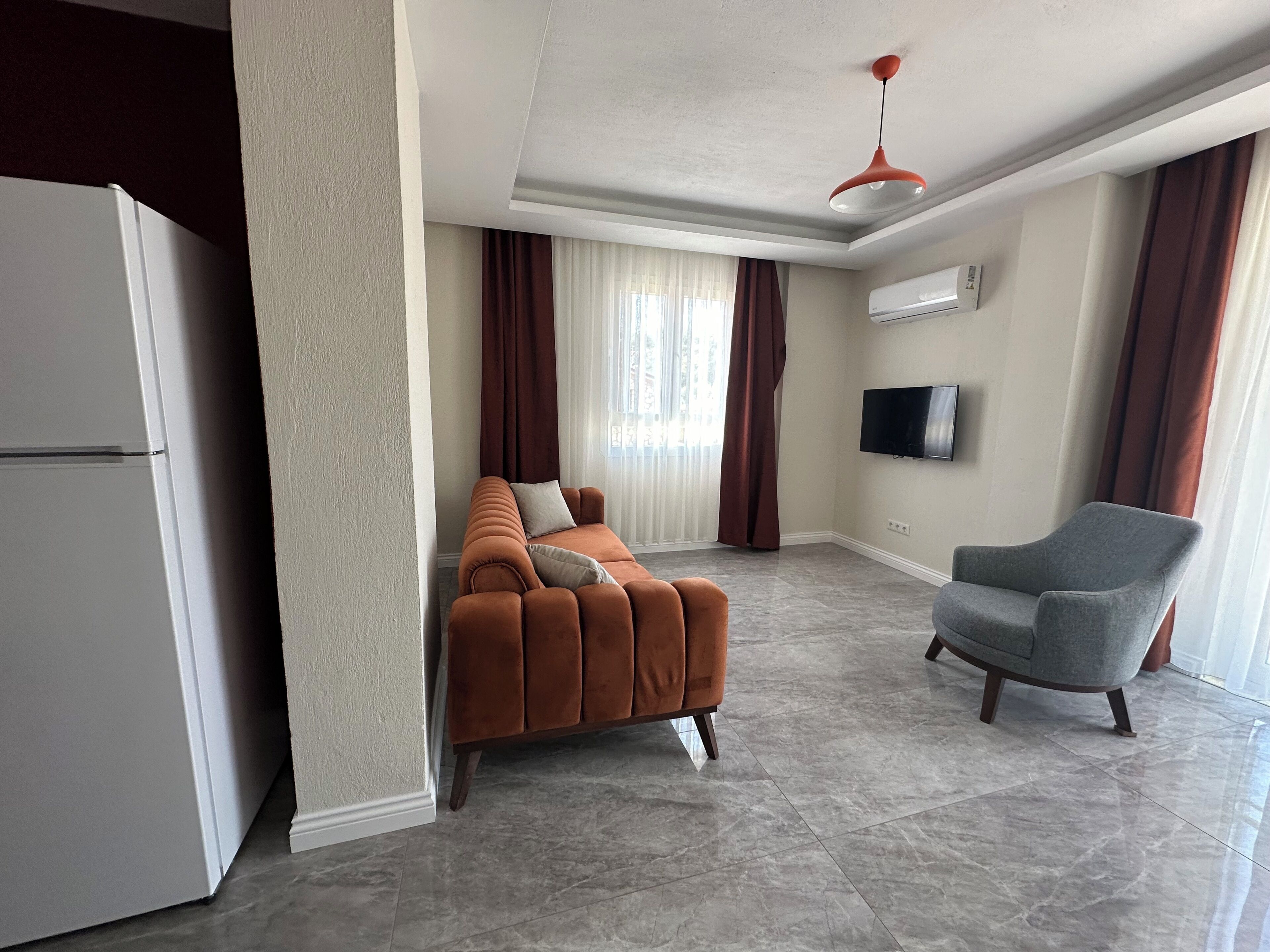 A modern living room with a sofa, armchair, flat-screen TV, and air conditioning unit.