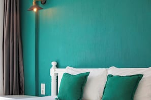 Een wand in zachte blauwgroene tint, een wit hoofdbord en twee groene kussens.