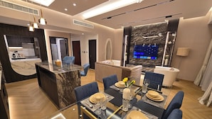 A modern dining area with a glass table, blue upholstered chairs, and a marble island with a kitchen in the background. - Highend Luxury Rimal with JBR view (Dubai)