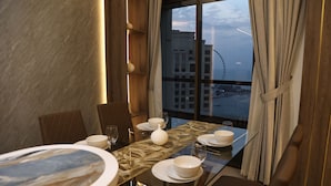 A dining area with a table set for four, a large window with curtains, and a view of buildings and a Ferris wheel. - Highend Bahar Ultra Luxury Stay (Dubai)