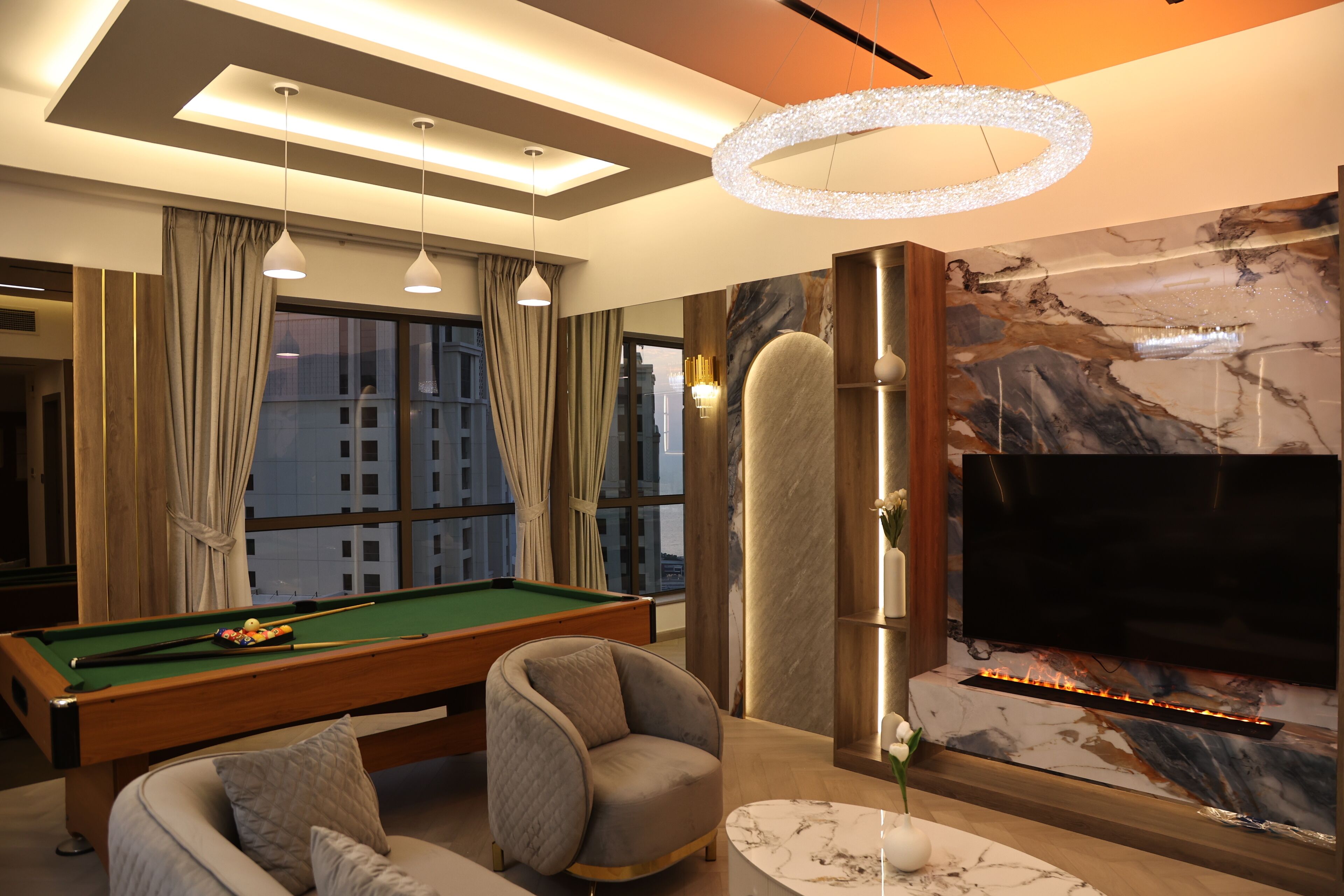 A modern living room with a pool table, comfortable seating, a large TV, and a fireplace.