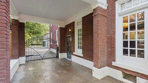 En overdækket indgang med en murstensfacade, en hegnet indkørsel og et vindue med mange ruder.