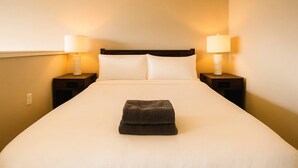 A hotel room with a large bed, two bedside tables with lamps, and a window on one side. - Forest Park Skyline Retreat with Balcony, Pool & Parking (St. Louis)