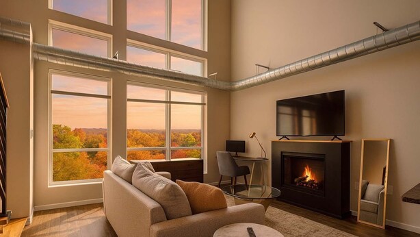 A spacious living room with a fireplace, large windows, and a flat-screen TV. - Forest Park Skyline Retreat with Balcony, Pool & Parking (St. Louis)