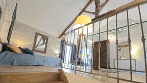 A staircase leading to a room with a bed, a glass railing, and a lamp. - Cozy apartment in the heart of Brantôme, private terrace (Brantôme en Périgord-Brantôme en Périgord)