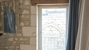 A room with a stone wall, a white door with a metal gate, and a blue curtain. - Cozy apartment in the heart of Brantôme, private terrace (Brantôme en Périgord-Brantôme en Périgord)