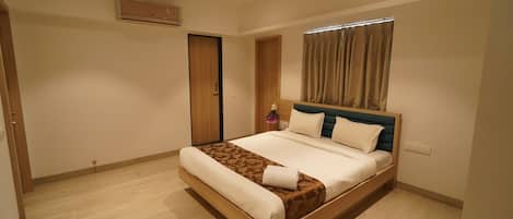A modern bedroom with a large bed, wooden flooring, a ceiling fan, and a window with curtains.